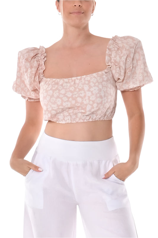 A woman wearing a cropped eyelet top with puffy sleeves and a ruffled square neckline, in a floral print, paired with white pants.