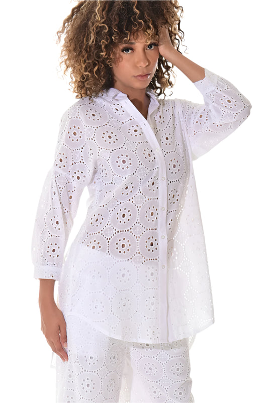 A female model wearing a white long-sleeved, V-neck, button-down cotton blouse with embroidered eyelets.
